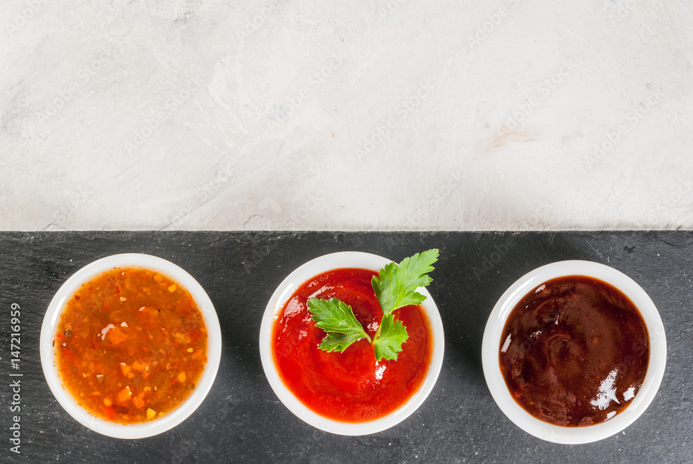 Three kinds of red tomato sauce on a white stone table: traditional classic ketchup, barbecue sauce, sweet and sour Chinese sauce. Top view copy space Three kinds of red tomato sauce on a white stone table: traditional classic ketchup, barbecue sauce, sweet and sour Chinese sauce. Top view copy space