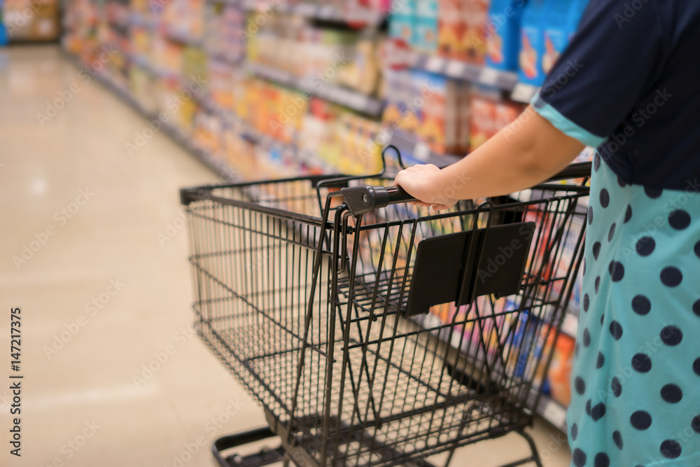 Female Hand Close Up With Shopping Cart in a Supermarket Walking Trough the Aisle,trolley in department store bokeh background,vintage color,copy space