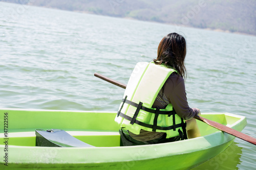  young woman equip life jacket sitting relaxing on prow have peddle on lap herself. she looking side around herself have sea and sunset background. this image for nature,travel and portrait photo