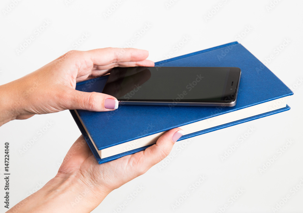 Closeup of young caucasian female hands holding modern smartphone and blue book isolated on white background. Choice concept. Horizontal color photo. Closeup of young caucasian female hands holding modern smartphone and blue book isolated on white background. Choice concept. Horizontal color photo.