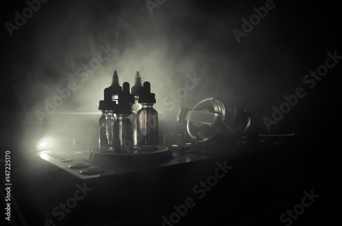 Vape and DJ Club concept. Smoke clouds and vape liquid bottles on Dj mixer close up. Light effects. Useful as background or vape or club advertisement or vape background.