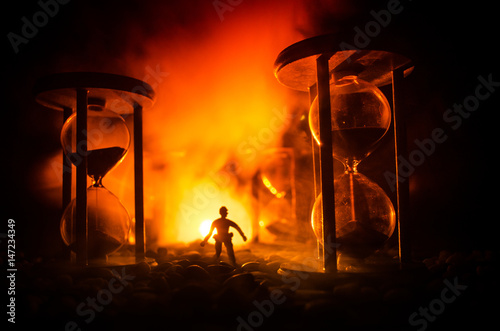 Time concept. Silhouette of a man standing between hourglasses with smoke and lights on a dark background.