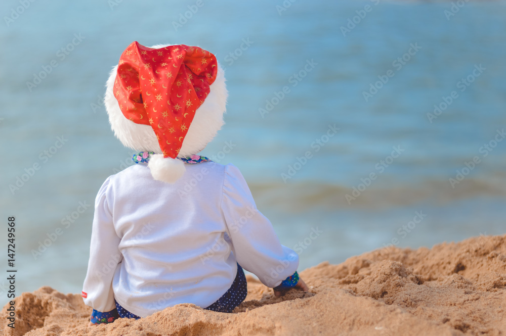 Little child in Santa Claus hat on sundy beach outdoors background. Back view picture Little child in Santa Claus hat on sundy beach outdoors background. Back view picture