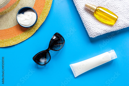 Summer cosmetic with protection cream and hat blue background top view