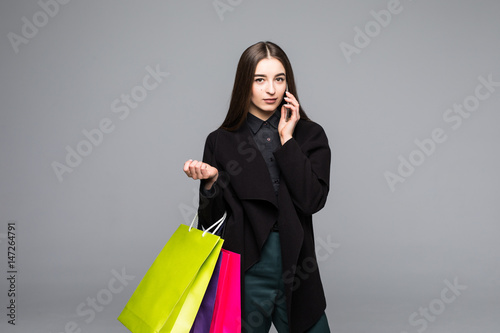 Happy female in white dress shopping, carry colored paper bags, talking on the cell phone, holding smartphone, making call, dreamily smiling.