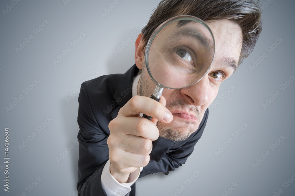 Young businessman is looking through magnifying glass. View from top. Young businessman is looking through magnifying glass. View from top.