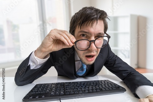 Картината върху платно Confused or unsure man is working with computer and looking at you