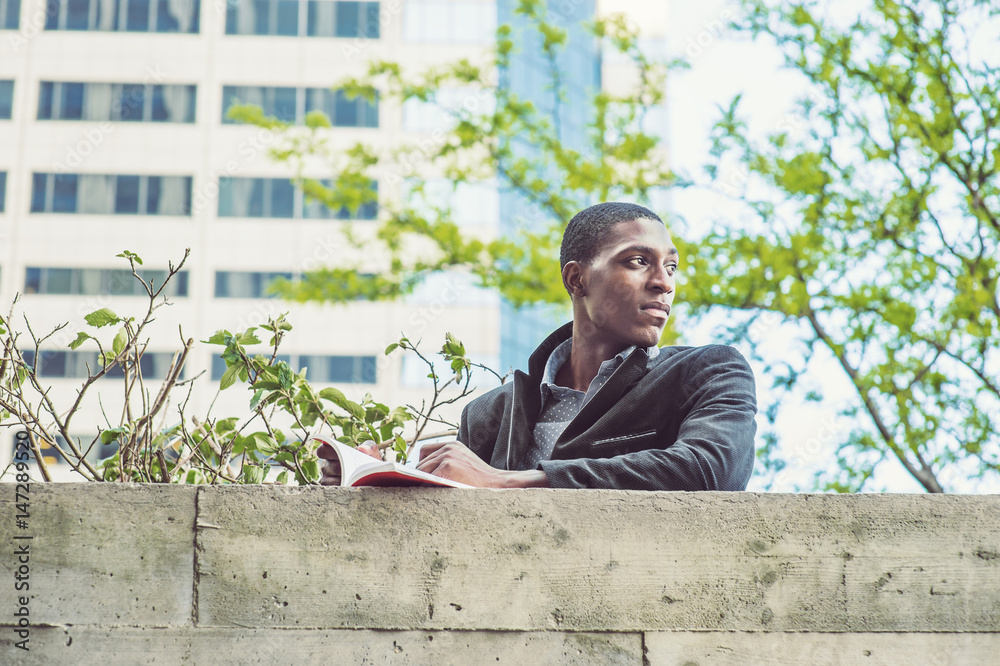 Young African American Man reading book on top of wall in New York Young African American Man reading book on top of wall in New York