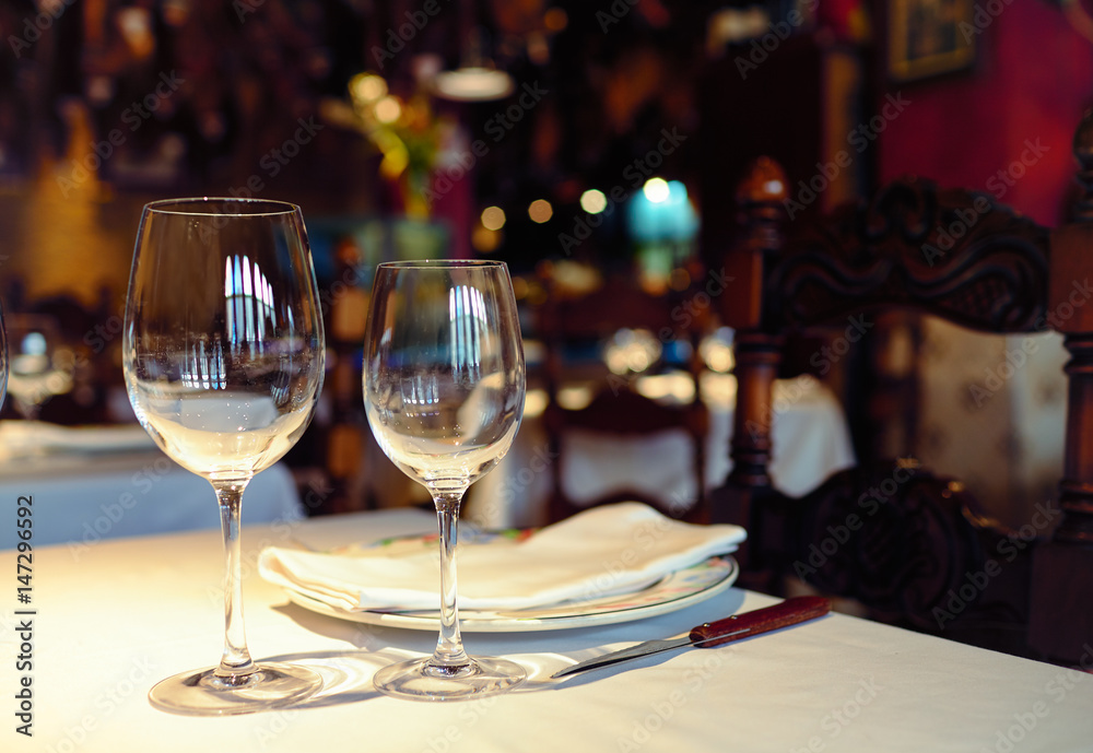 Empty glasses in a restaurant on white tablecloth. Shade, brown background and carved chairs.