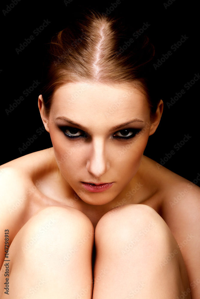 Young nude woman with dark eye make up sitting on the floor