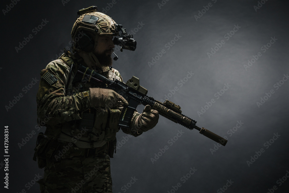 Bearded soldier in Combat Uniforms with weapon, plate carrier and combat helmet are on. Studio shot, dark background Bearded soldier in Combat Uniforms with weapon, plate carrier and combat helmet are on. Studio shot, dark background