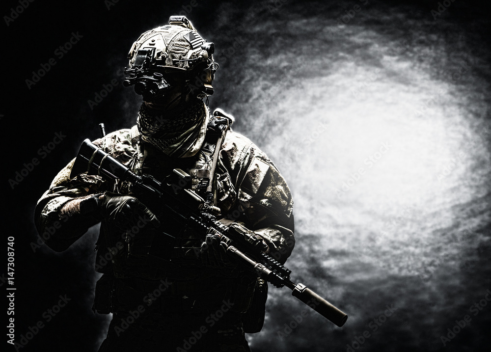 Army soldier in Combat Uniforms with assault rifle, plate carrier and combat helmet are on, Shemagh Kufiya scarf on his neck. Studio shot, dark background Army soldier in Combat Uniforms with assault rifle, plate carrier and combat helmet are on, Shemagh Kufiya scarf on his neck. Studio shot, dark background