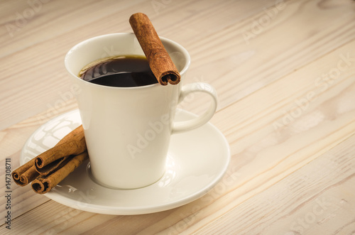 cup of coffee with cinnamon on a light tree/white cup of coffee with cinnamon sticks on a light tree