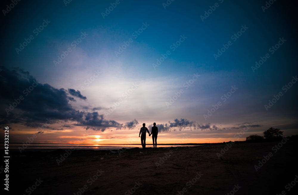 Silhouettes of woman and man on a background of colorful sunset of a cloudy day on the beach 