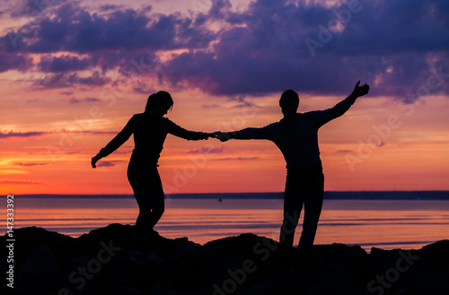 Silhouettes of woman and man on a background of colorful sunset of a cloudy day on the beach 