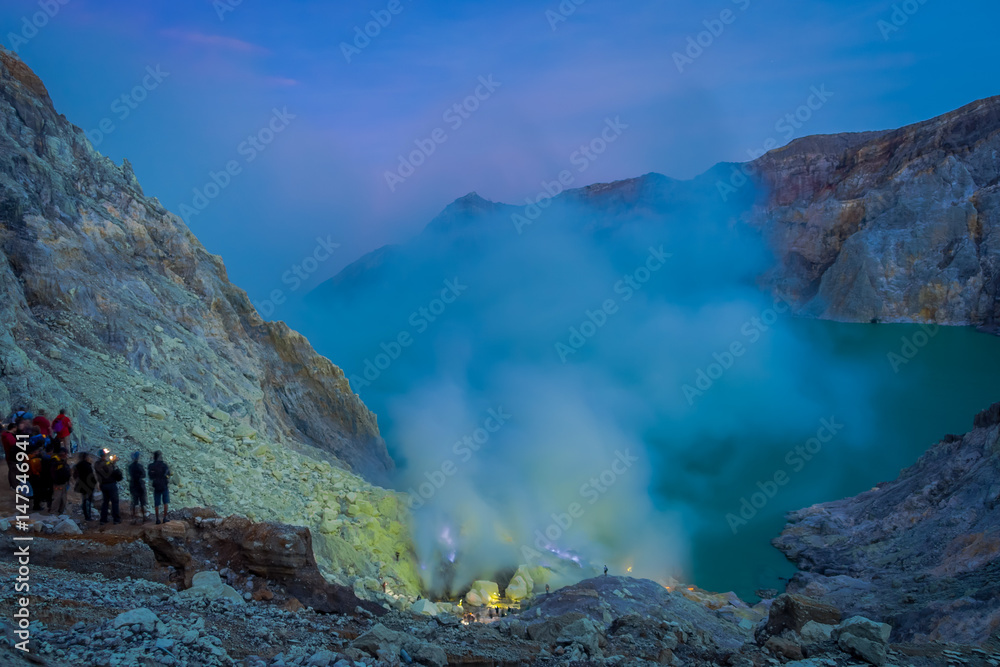 Obraz premium KAWEH IJEN, INDONESIA: Nice overview of sulfur mine with miners working next to volcanic crater lake, spectacular nature