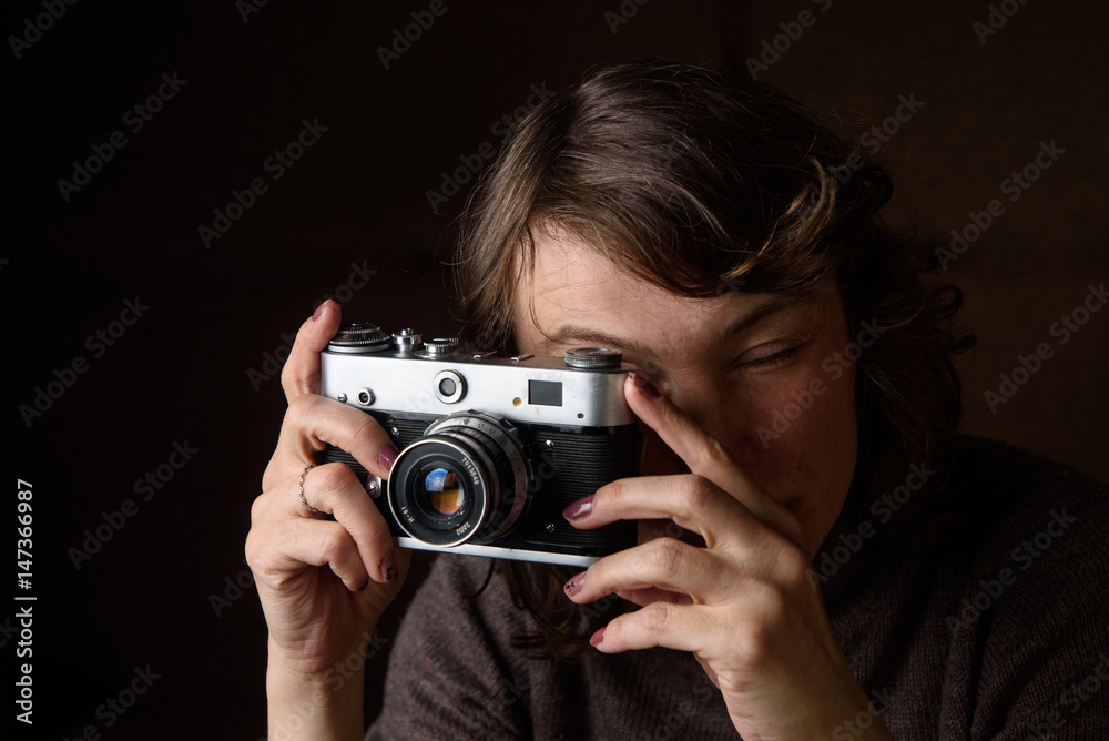 A woman is photographing a retro camera on a dark background.
A woman is photographing a retro camera on a dark background.