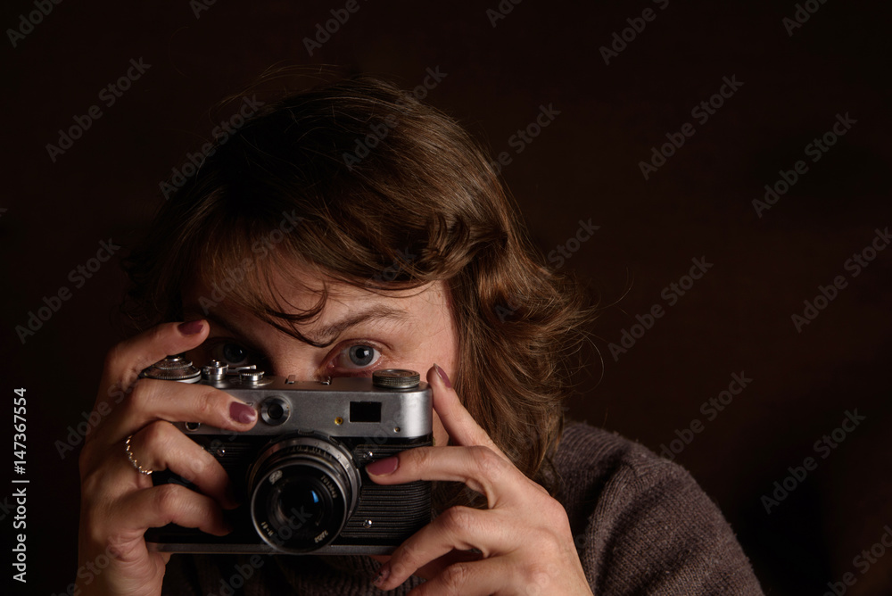 A woman is photographing a retro camera on a dark background.
A woman is photographing a retro camera on a dark background.