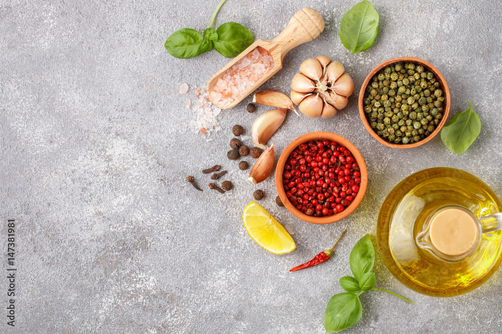Selection of spices and herbs - garlic, salt, pink, green and black pepper, lemon, Basil, olive oil. Ingredients for cooking. Food background on grey  table slate. Top view copy space