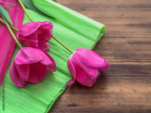 Fototapeta Naklejka Na Ścianę i Meble -  Pink tulips, floral arrangement on wooden background with green paper and space for message. Background for Mother's Day, 8 March and other greeting cards or invitations for lovely women. Soft focus.