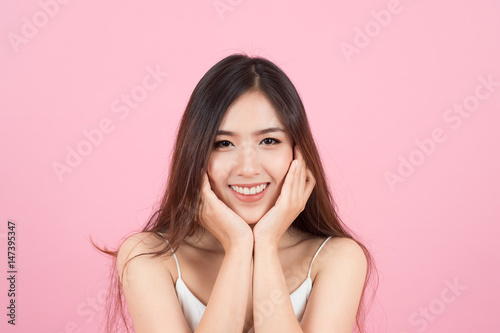 Asian young beautiful woman smiling and touch her face like a v-shape isolated over pink background. Cleaning face, perfect skin. SPA therapy, skincare, cosmetology and plastic surgery concept