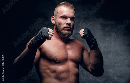 Studio portrait of brutal bearded fighter over dark grey background. © Fxquadro