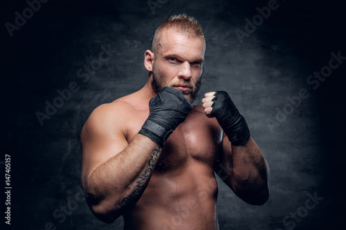 Studio portrait of brutal bearded fighter over dark grey background. © Fxquadro