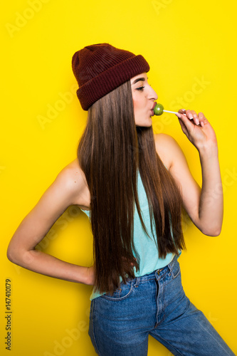 hipster girl bite lollipop on yellow background