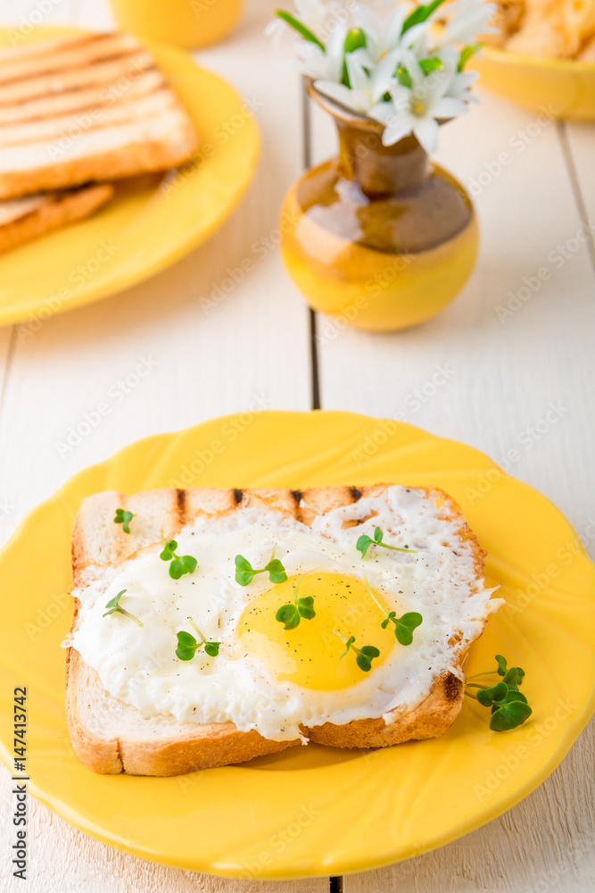 Toast with egg in yellow plate near vase with flower on white wooden background. Healthy breakfast.