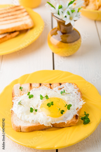 Toast with egg in yellow plate near vase with flower on white wooden background. Healthy breakfast.