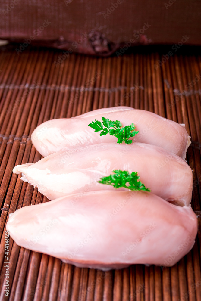 Raw chicken fillet with parsley on wooden background.