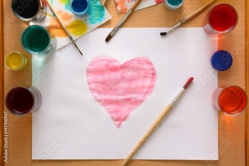 Watercolor heart on white paper among creative chaos on the table