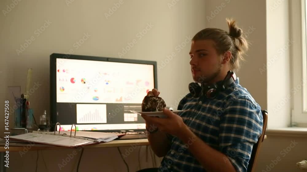 Young man eating dessert in the office and smiling to the camera
Young man eating dessert in the office and smiling to the camera