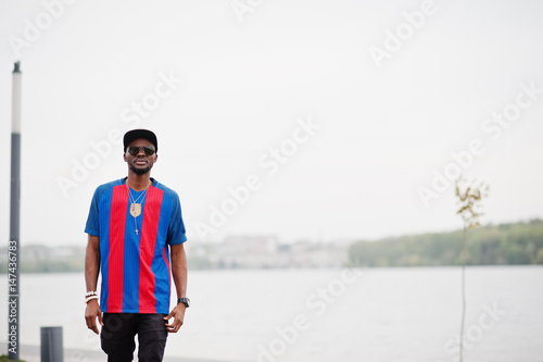 Stylish african american boy wear at cap, football t-shirt and sunglasses. Black sports man portrait. © AS Photo Family