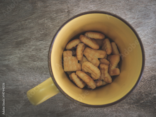Top view letter biscuit in yellow cup on wooden background