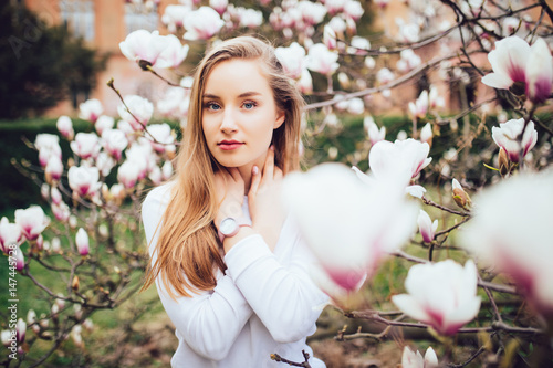 lovely girl standing near Magnolia blossoming flowers, stands in white pink dress a small smile smiling photo