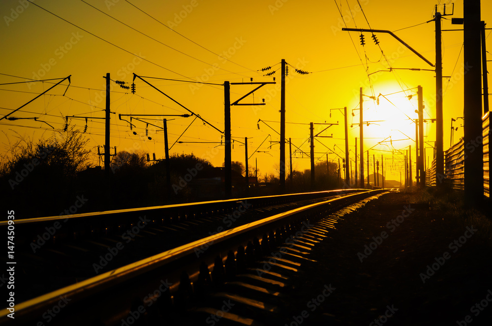 Railway - Railroad at sunset with sun, Rails and electric lines in yellow light Railway - Railroad at sunset with sun, Rails and electric lines in yellow light