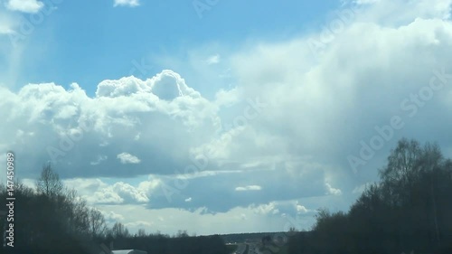 Bright fluffy clouds at blue sky, car ride at wood margin, look up 
