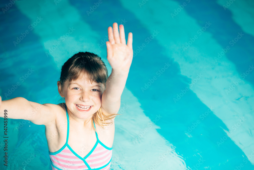 Happy little girl waving in swim pool