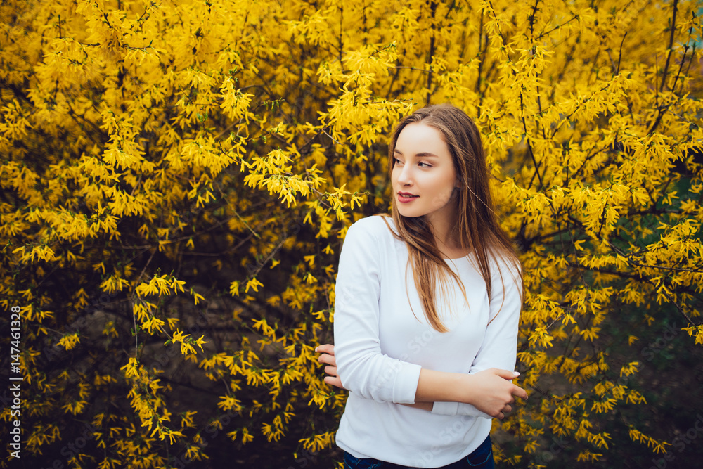 Woman standing in front of yellow blooming tree in city street in spring day Woman standing in front of yellow blooming tree in city street in spring day