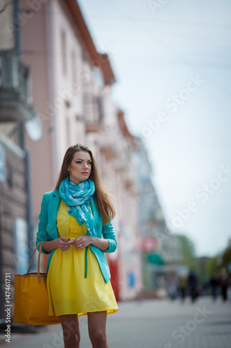 Beautiful brunette young woman wearing nice dress  yellow handbag  walking on the street. Fashion city photo.