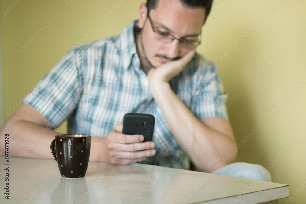 Man sitting at table with cup of coffee in front of him and checking his mobile phone Man sitting at table with cup of coffee in front of him and checking his mobile phone
