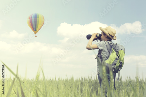 Child looks curious with his binoculars a hot air balloon flying in the sky