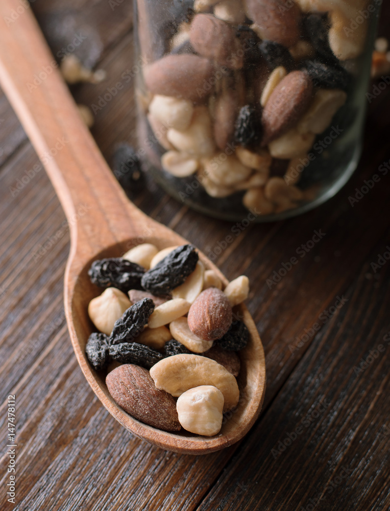 Fototapeta premium Spoon with jar full of nuts and raisins on a wooden background. Cloae up.