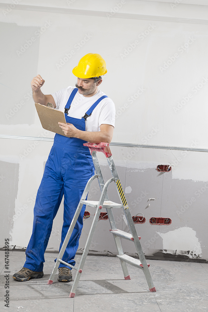 Construction worker wearing overalls and helmet taking notes on clipboard. Construction worker wearing overalls and helmet taking notes on clipboard.