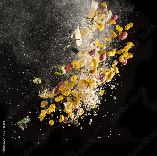 Ingredients for Italian kitchen (tomato, pasta, cheese, chopping board and knife) isolated in the air on black background, freeze motion image