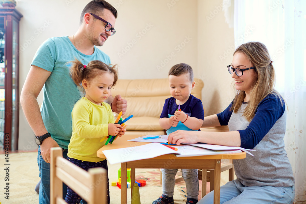 The family draws pencils at a table in room. The family draws pencils at a table in room.