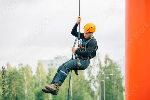 Obraz na płótnie Industrial climber in uniform and helmet rises. Risky job. w salonie