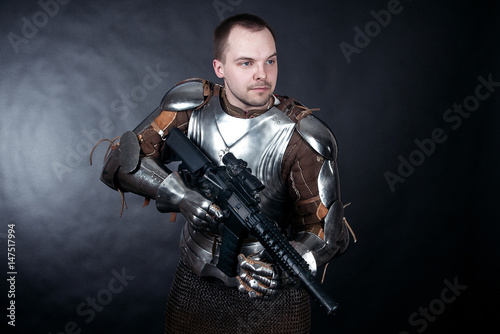 A medieval warrior with firearms. Knight with assault rifle on dark background