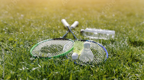 Two badminton rackets and a bottle of water shot at sunset